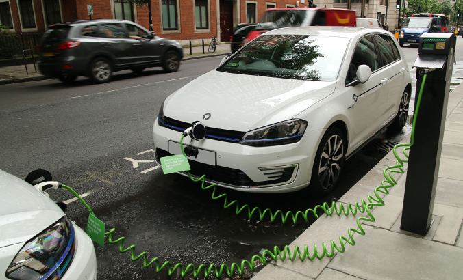 两辆现代电动汽车在伦敦繁忙的街道上停在一个充电站时，为电池充电，从而减少了污染和气候变化