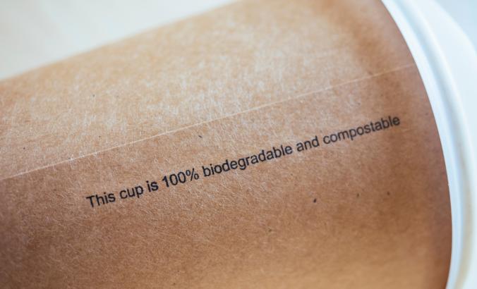 在棕色咖啡杯上，带有黑色写作，上面写着：“这个杯子是100％可生物降解且可堆肥的”“loading=